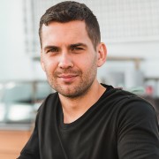 Slightly smiling man with short dark hair and scruffy facial hair